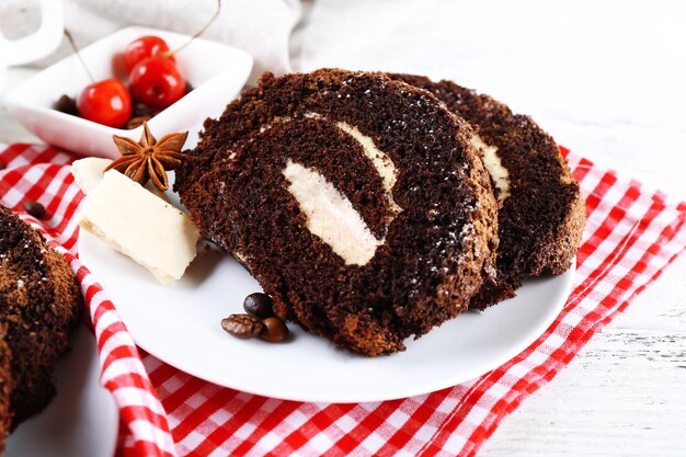 Delicioso rollo de chocolate en platillo blanco en primer plano de servilleta a cuadros