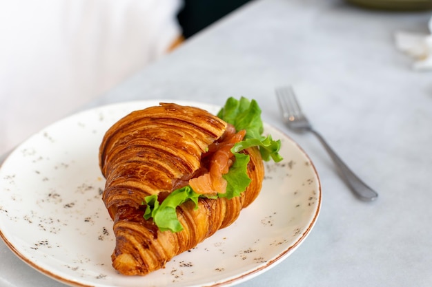 Delicioso y saludable croissant de desayuno con lechuga de salmón y queso crema en un plato