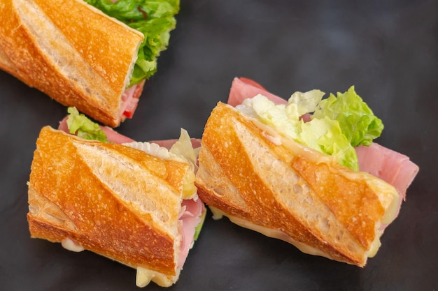 Delicioso sanduíche de presunto com queijo e alface em um prato preto cozido em um restaurante