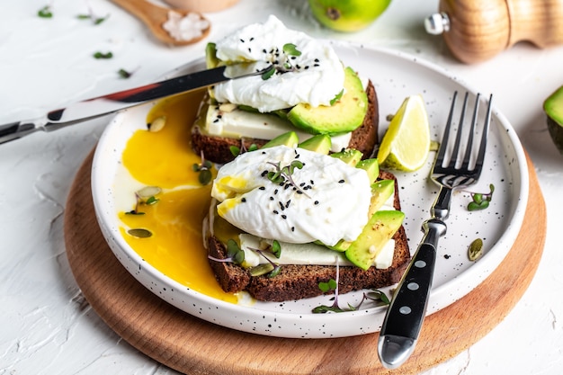 Delicioso sándwich con aguacate y huevo escalfado en una tabla de cortar de madera, delicioso desayuno o almuerzo saludable