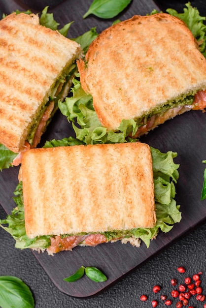 Delicioso sándwich crujiente con tostadas de salmón, aguacate, tomates, sal, especias y hierbas sobre un fondo de hormigón oscuro