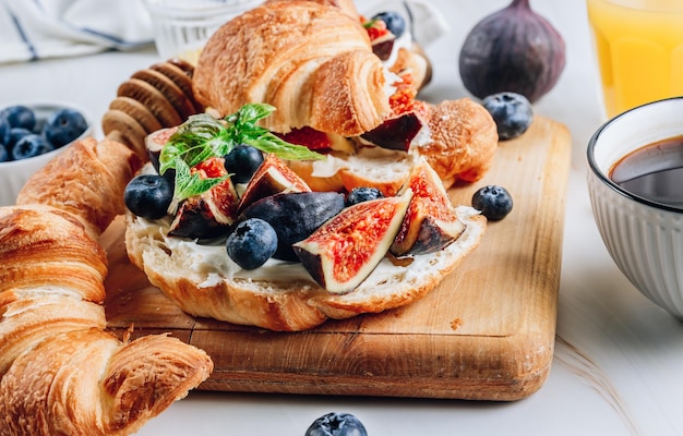 Delicioso sándwich dulce con croissants, queso suave, arándanos e higos sobre fondo de mármol Concepto de desayuno con café y jugo de oranfe Enfoque selectivo