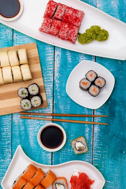 Delicioso set de sushi Nigiri servido con salsa de soja tradicional y palillos, plano sobre mesa de madera azul. Sabrosos mariscos japoneses, vista superior