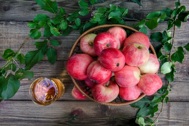 Delicioso suco de maçã em um copo e lindas maçãs vermelhas em um prato de vime em uma vista superior de fundo rústico de madeira