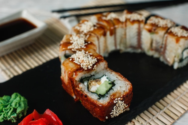 Delicioso sushi fresco, rollo de dragón dorado uramaki servido en pizarra negra, sobre fondo de estera de paja, primer plano. Comida tradicional japonesa.