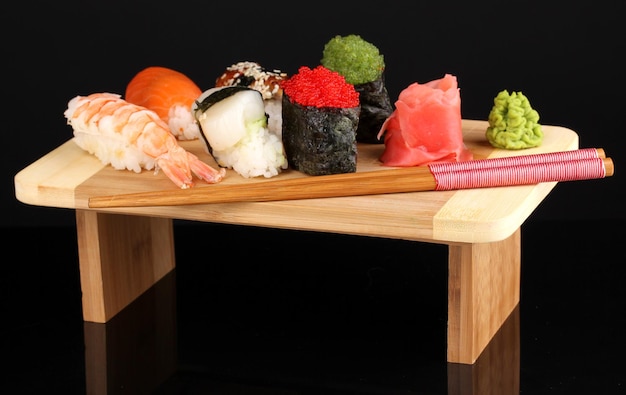 Delicioso sushi servido en tablero de madera aislado en negro