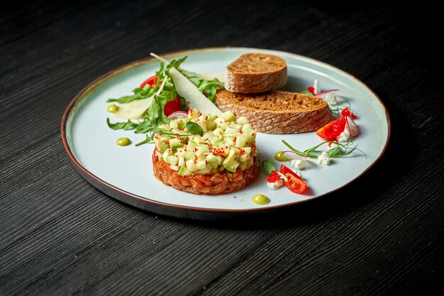 Delicioso tártaro de salmão com abacate e croutons em um prato. fundo de madeira. Foco seletivo