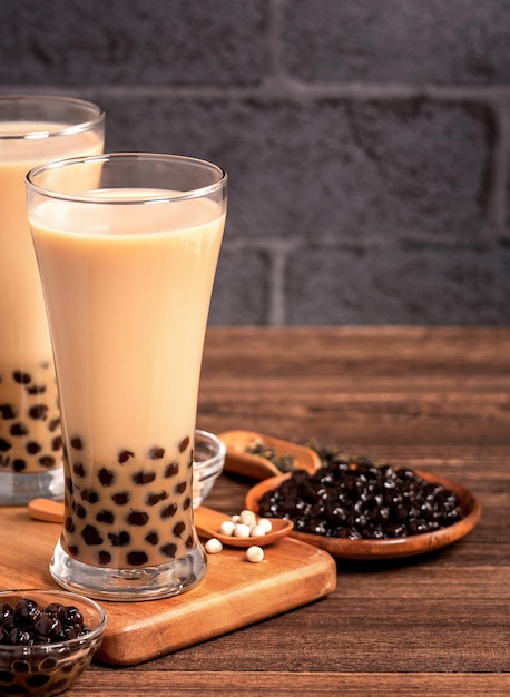 Delicioso té con leche de burbujas con bola de perla de tapioca en vidrio sobre mesa de madera y fondo de ladrillo gris oscuro comida y bebida popular en Taiwán cerca