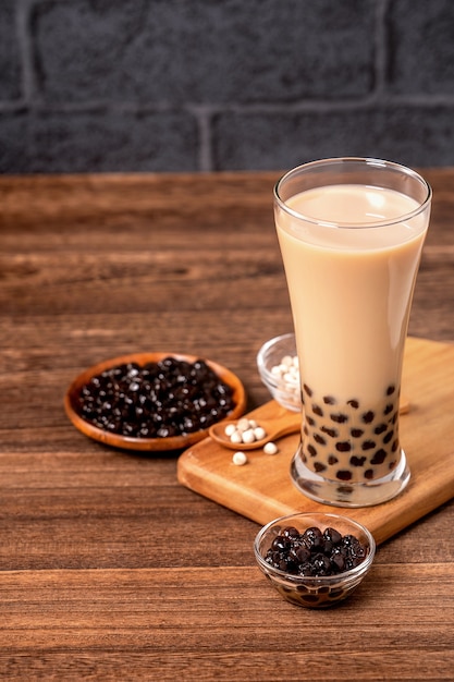 Delicioso té con leche de burbujas con bola de perlas de tapioca en vidrio sobre mesa de madera