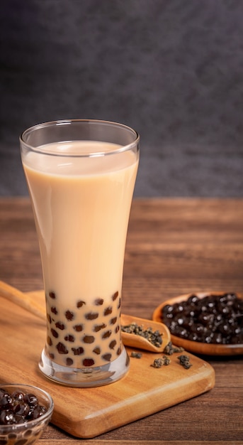 Delicioso té con leche de burbujas con bola de perlas de tapioca en vidrio sobre mesa de madera