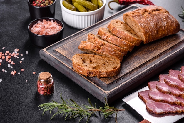 Delicioso tocino fresco en rodajas con pan y verduras sobre un fondo de hormigón oscuro