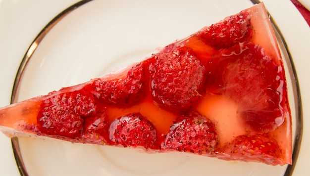 Delicioso trozo de tarta de queso de fresa en un plato blanco, sobre la mesa con una servilleta a cuadros rojos, vista superior.