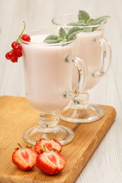 Delicioso yogur de fresa con hojas de menta en vasos y fresas frescas en la tabla de cortar de madera