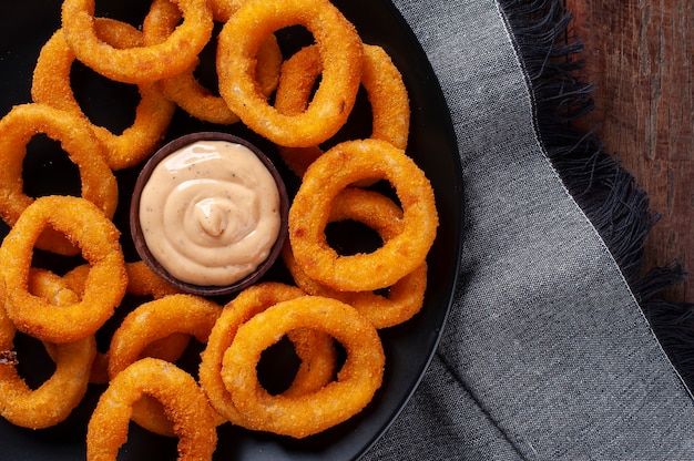 Deliciosos anéis de cebola fritos crocantes caseiros com molho picante. Vista do topo. Copie o espaço