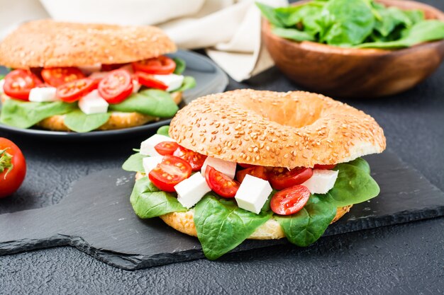 Deliciosos bagels listos para comer rellenos de tomate, feta y hojas de espinaca sobre un fondo negro. Refrigerio ligero y saludable