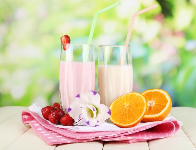 Deliciosos batidos de leche con fresas y naranja sobre mesa de madera sobre fondo natural