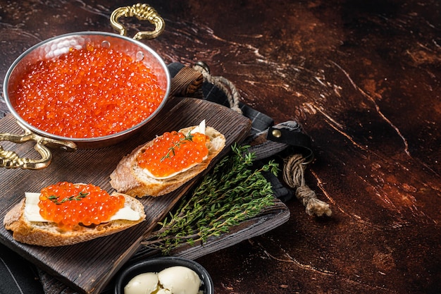 Deliciosos bocadillos con pescado Caviar rojo sobre tabla de madera. Fondo oscuro. Vista superior. Copie el espacio.