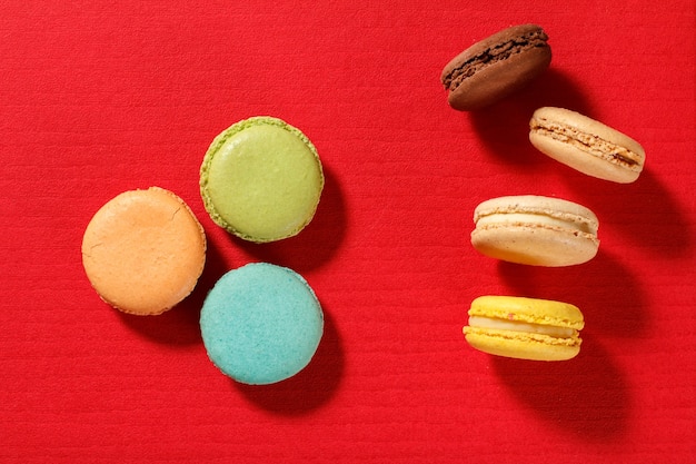 Deliciosos bolos de macarons de cor diferente na superfície texturizada vermelha. Vista do topo