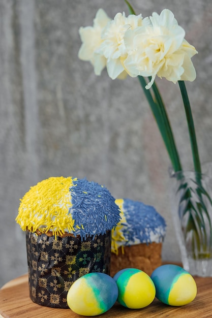 Deliciosos bolos de Páscoa nas cores da bandeira da Ucrânia ovos de Páscoa de cor amarelo-azul em uma mesa de madeira com flores no lugar de fundo para foco seletivo de texto