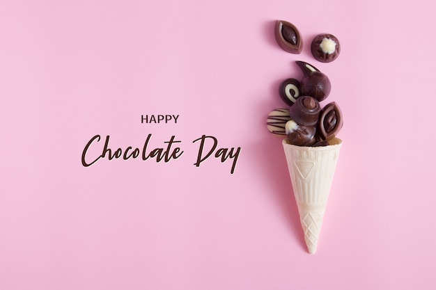 Deliciosos bombons de chocolate em casquinha de waffle na superfície rosa com a inscrição feliz dia do chocolate