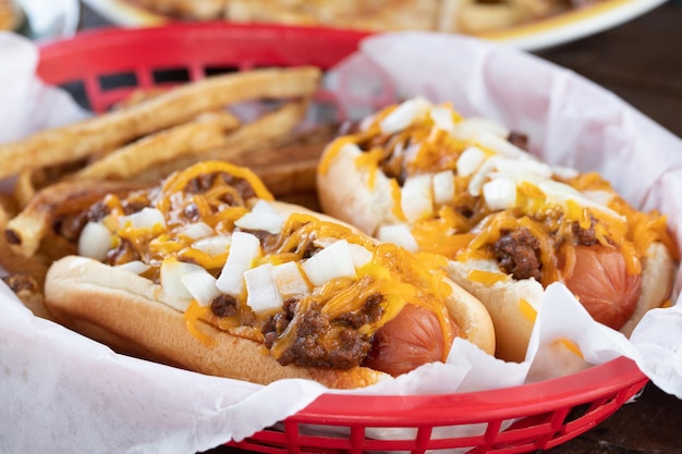 Foto deliciosos cachorros-quentes decorados com cebola, carne e queijo cheddar derretido e batatas fritas