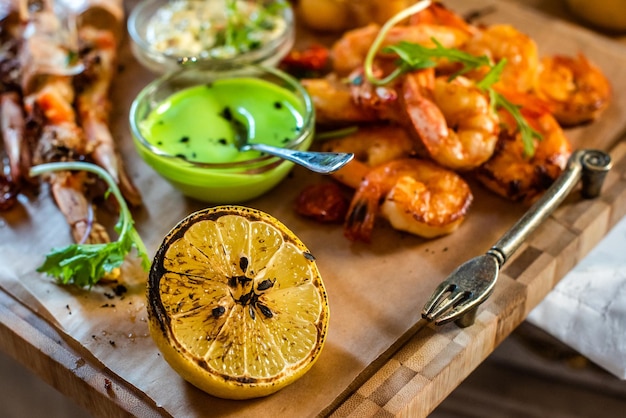 Deliciosos camarões assados com frutos do mar grelhados para churrasco de limão com molhos em uma travessa de madeira