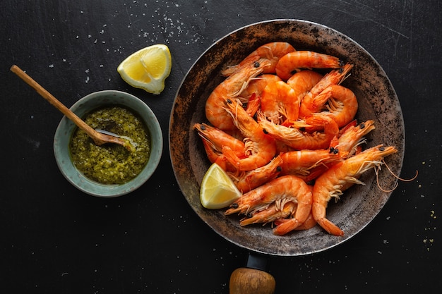 Deliciosos camarones con especias y salsa en sartén sobre superficie oscura