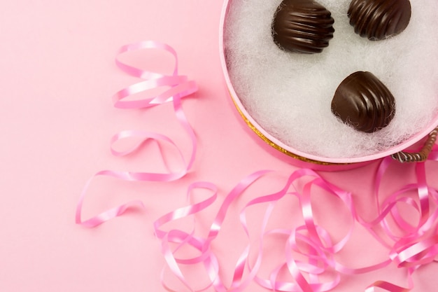 Deliciosos caramelos de chocolate en una caja sobre un fondo rosa.
