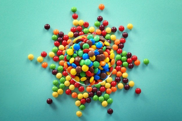 Deliciosos caramelos de colores en un recipiente sobre la superficie de color