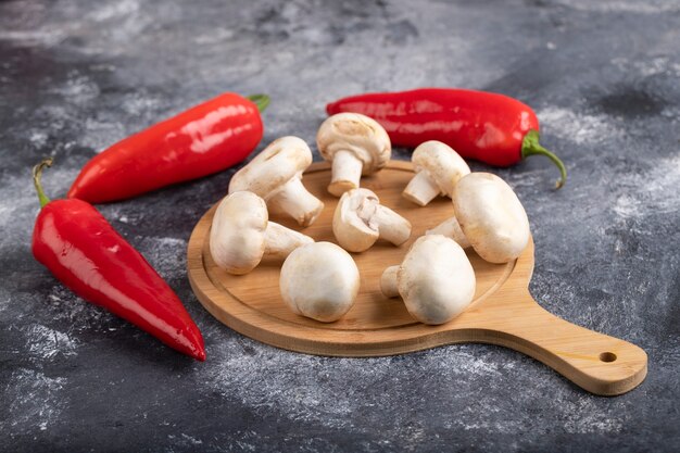 Deliciosos champiñones blancos crudos con chiles en la superficie de mármol.