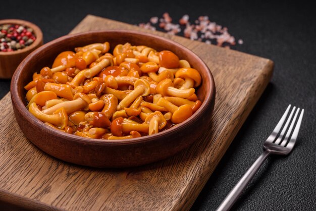 Deliciosos champiñones encurtidos con sal y especias en un plato de cerámica sobre un fondo de textura oscura