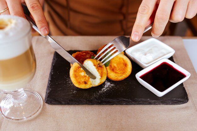 Deliciosos cheesecakes caseiros cortados com um garfo polvilhado sirnik café da manhã com bolos de queijo e café o homem está comendo um doce café da manhã cheesecakes com geléia no café da manhã são cortados com uma faca