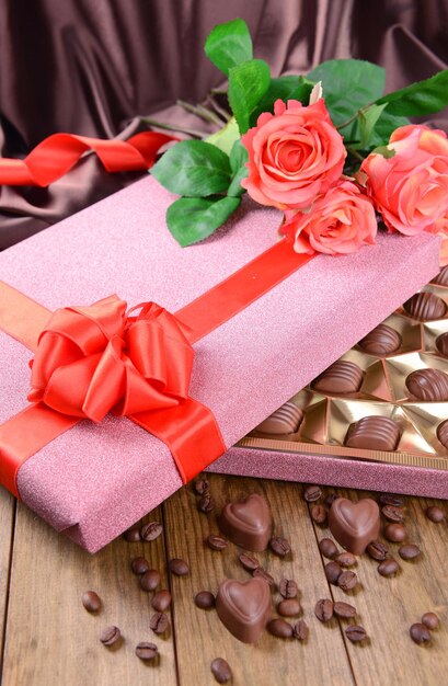 Deliciosos chocolates en caja con flores en la mesa sobre fondo marrón