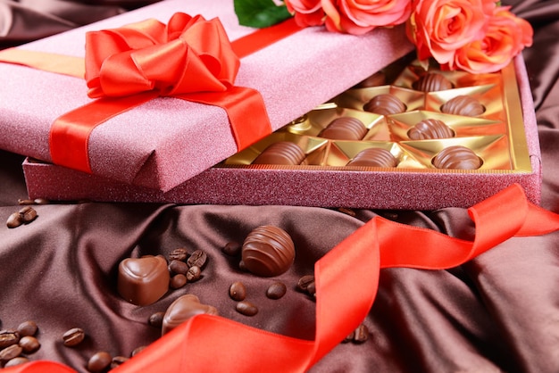 Deliciosos chocolates em caixa com flores em fundo marrom