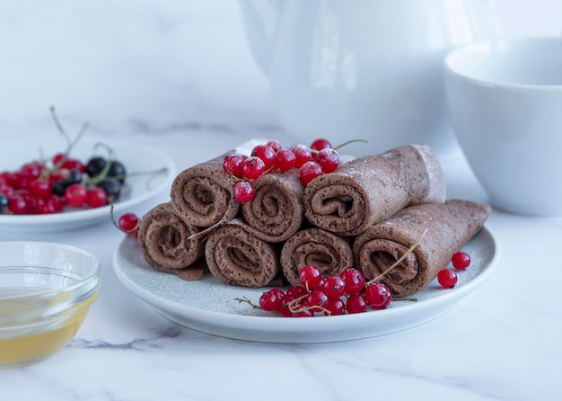 Deliciosos crepes de chocolate enrollados en rollos adornados con azúcar en polvo y grosellas rojas