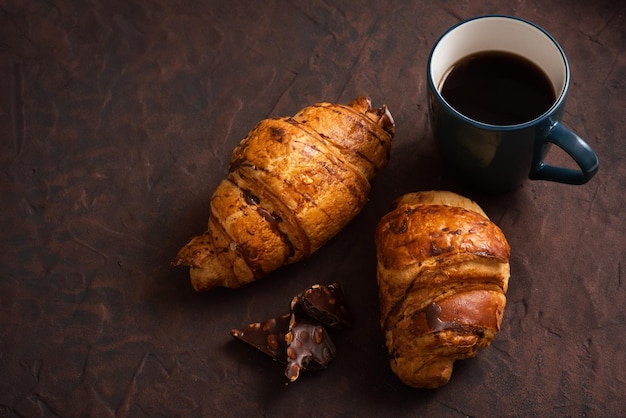 Foto deliciosos croissants crocantes café quente de chocolate no copo azul no prato na mesa escura café da manhã saboroso