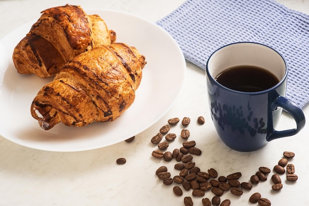 Deliciosos croissants crocantes deliciosos café quente na xícara azul e toalha de cozinha no prato na mesa de mármore