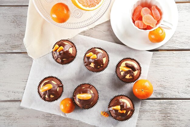 Deliciosos cupcakes con rodaja de mandarina y chocolate en un papel sobre fondo de madera clara