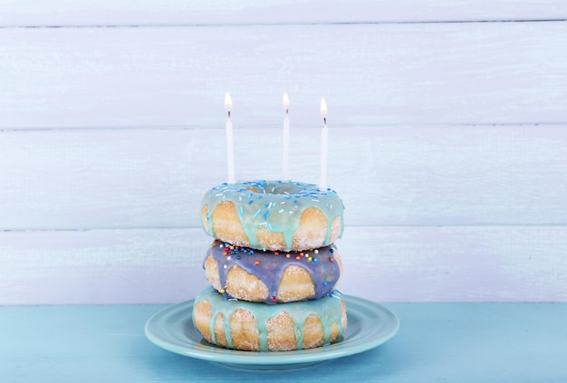 Deliciosos donuts com glacê e velas de aniversário na mesa com fundo de madeira