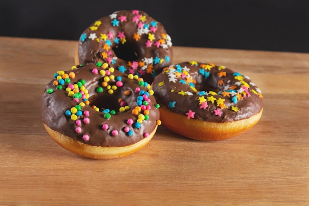 Deliciosos donuts em uma base de madeira e fundo preto.