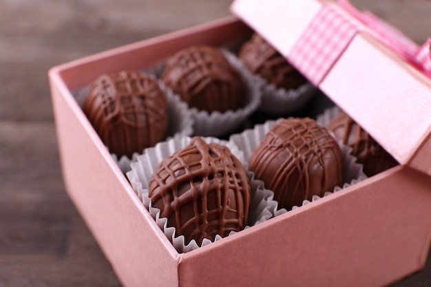 Deliciosos dulces de chocolate en caja de regalo rosa sobre fondo de madera, de cerca