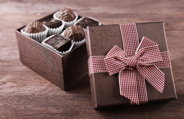 Deliciosos dulces de chocolate en una hermosa caja de regalo sobre fondo de madera