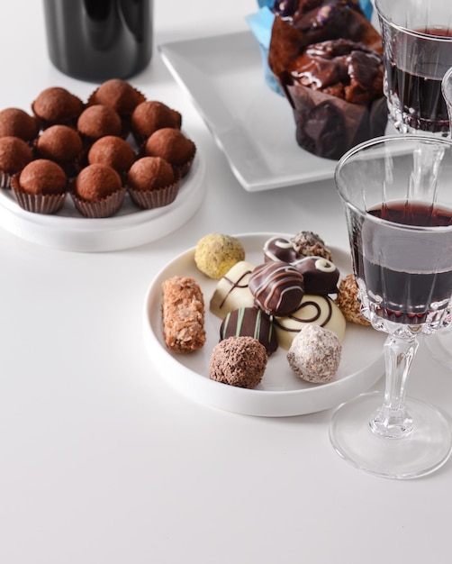 Foto deliciosos dulces de chocolate y vino tinto sobre fondo blanco.