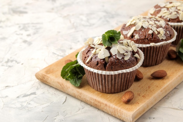 Deliciosos y dulces muffins de chocolate, con pétalos de almendra junto a menta y nueces de almendra sobre una mesa liviana de hormigón. de cerca