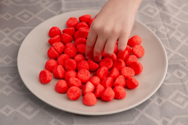 Deliciosos dulces rojos dispuestos en un plato mientras pequeñas manos se extienden en alegre anticipación de la dulce delicia