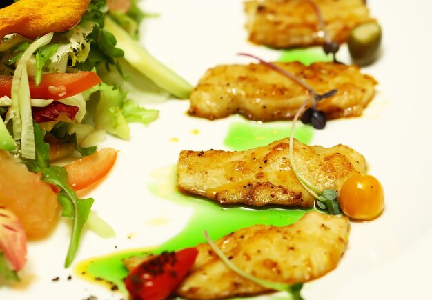 Deliciosos filetes de pescado frito y mezcla de ensalada verde con verduras frescas y coloridas en un plato sobre fondo blanco Gastronomía molecular moderna