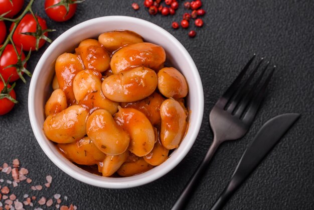 Foto deliciosos frijoles enlatados en tomate en un recipiente de cerámica blanca sobre un fondo de hormigón oscuro