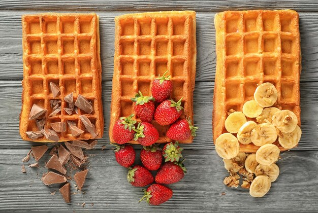 Deliciosos gofres con plátano, bayas y chocolate en la mesa de madera, endecha plana