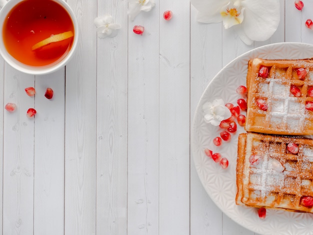 Deliciosos gofres vieneses deliciosos con miel y semillas de granada en un plato blanco