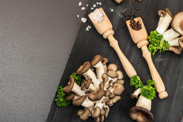 Foto deliciosos hongos ostra orgánicos con especias y perejil fresco en tabla de cortar de madera fuente de beta glucano piedra negra vista superior de fondo de hormigón